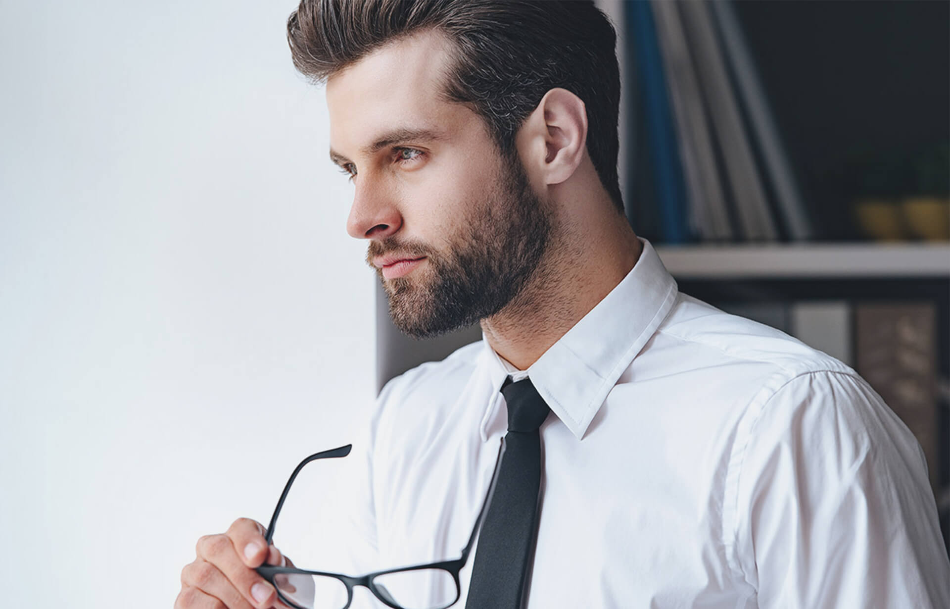 A professional man in a shirt and tie holds a pair of glasses, representing commercial lawyers in Perth.