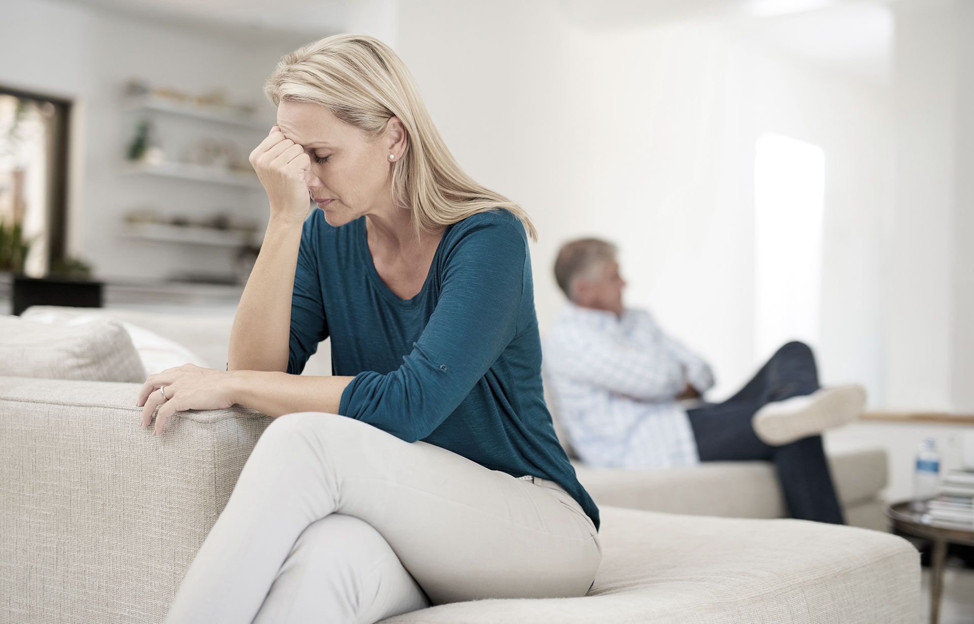 A distressed woman sits on a couch, her head in her hands, contemplating her next steps, potentially involving divorce lawyers in Perth.